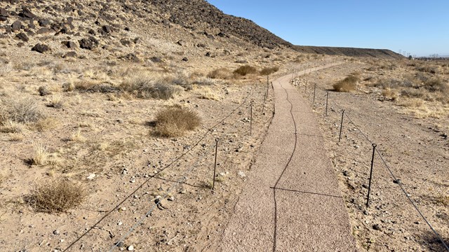 A trail surrounded by cables through a sandy volcanic landscape.
