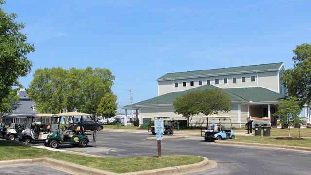 Multiple golf carts are parked in the lot next to the2-story visitor center