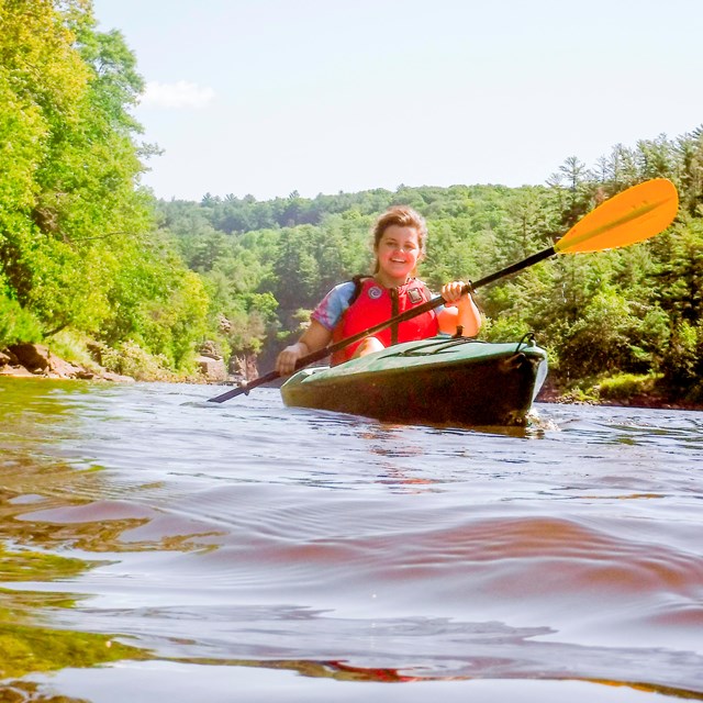 A kayaker paddles on a river with cliffs in the background.