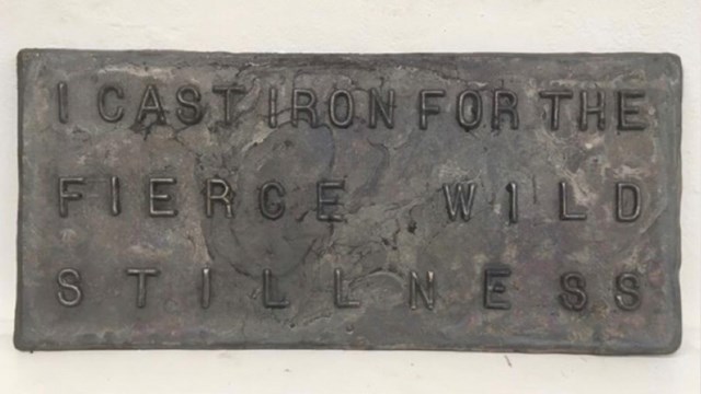 Cast iron plaque with the words "I cast iron for the fierce, wild stillness" on it