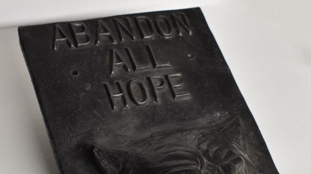 Cast iron art with the text " Abandon all Hope" written above a wolf's head
