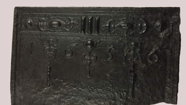 A cast iron fireback hung on fireplace meant to protect bricks from heat.