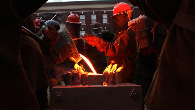 Several people wearing hard hats and facial shields surround a metal block.