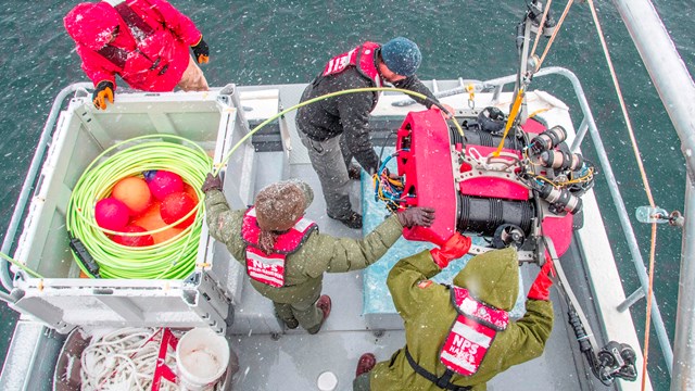 Overhead view of people deploying submersible survey equipment from the back of a boat.