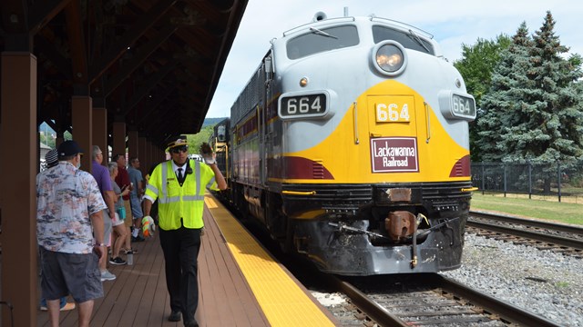 An employee walks on boarding platform next to gray and yellow diesel locomotive number 664