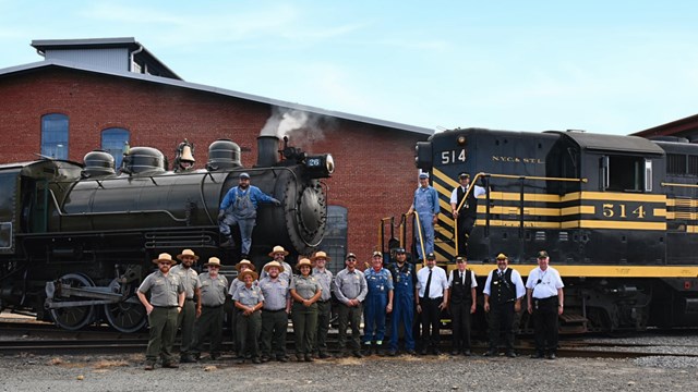 Two locomotives facing each other nose to nose, a group of employees pose in front of locomotives