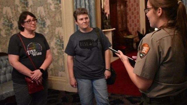 Two women are standing in a room while a ranger gives a tour.