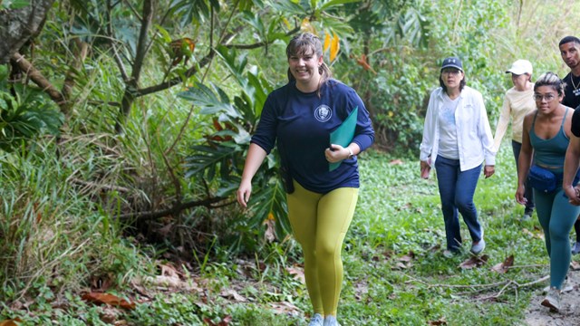 A woman in a blue shirt and yellow leggings leads a hike through the jungle