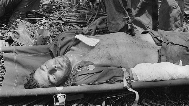 Soldier lying on a stretcher with his arm bandaged.