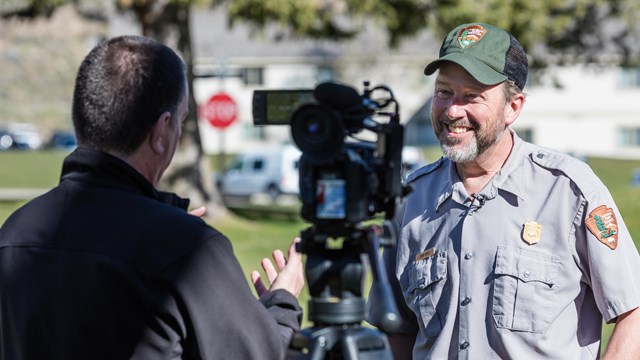 A park ranger is interviewed and filmed by a person standing behind a camera on a tripod.