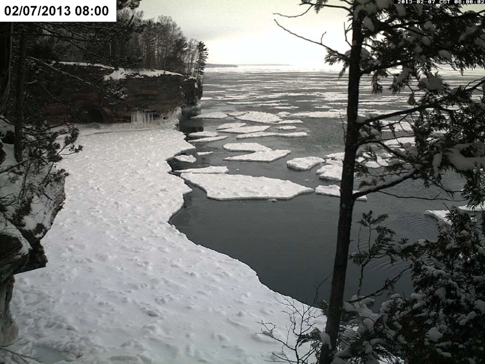 Upper left corner: White box with black text that reads 02/06/2013 17:00. A snow-covered frozen lake stretches between two cliffs and far out into the distance. No water visible.