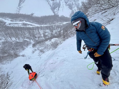 Brushing up on skills with Rigging for Rescue Two rangers on a snowy hillside pulling up orange rescue equipment