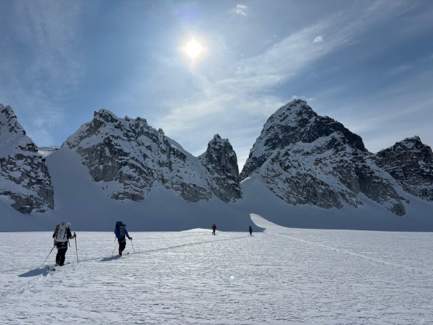Early season skiing on Glacier 1 Four skiers in a line across a snowy landscape with mountains and a blue sunny sky in the background
