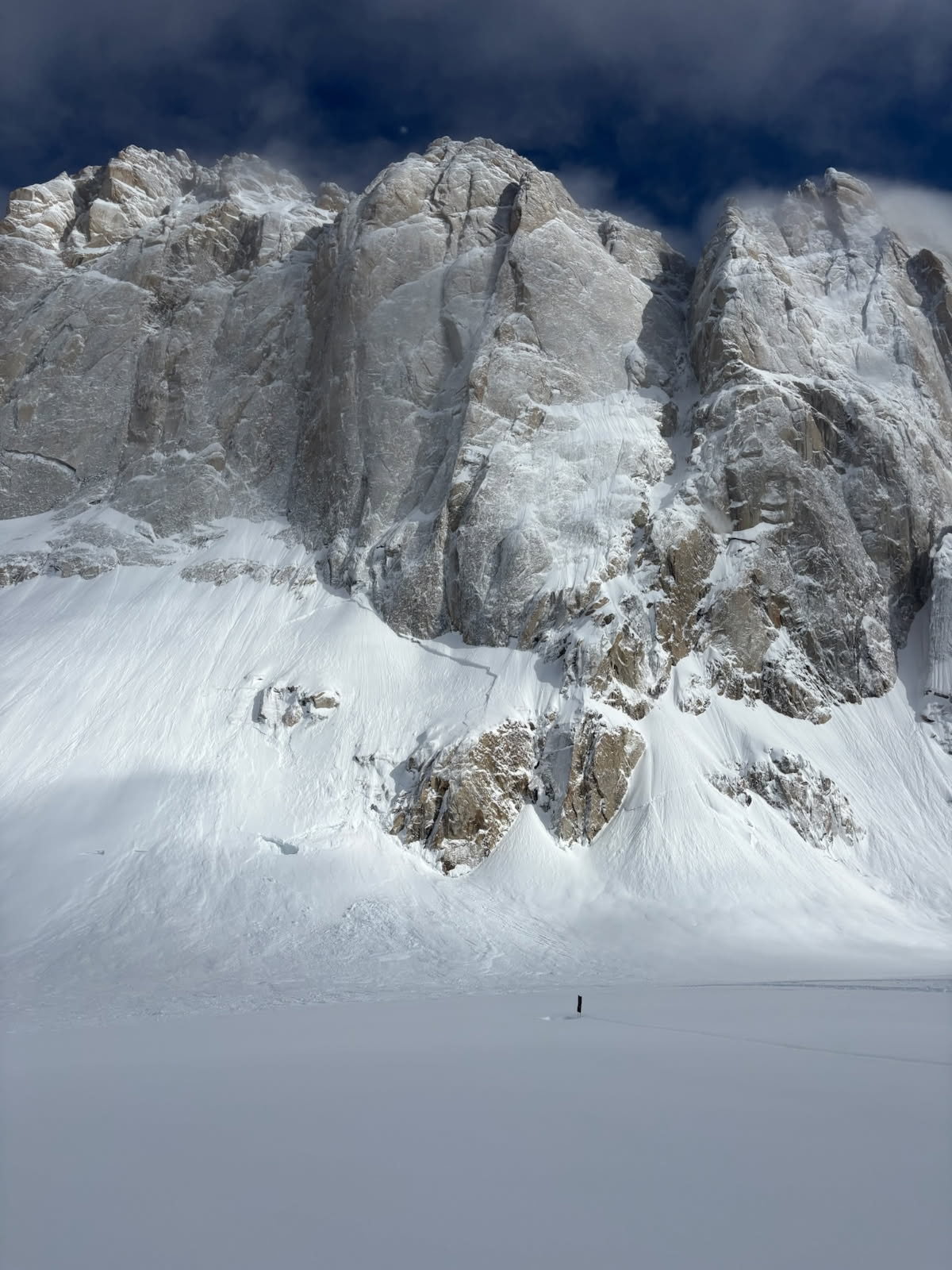 Ham and Eggs on the Mooses Tooth Large white mountain rockface above a snow covered area and a person who looks very small due to the size of the mountain