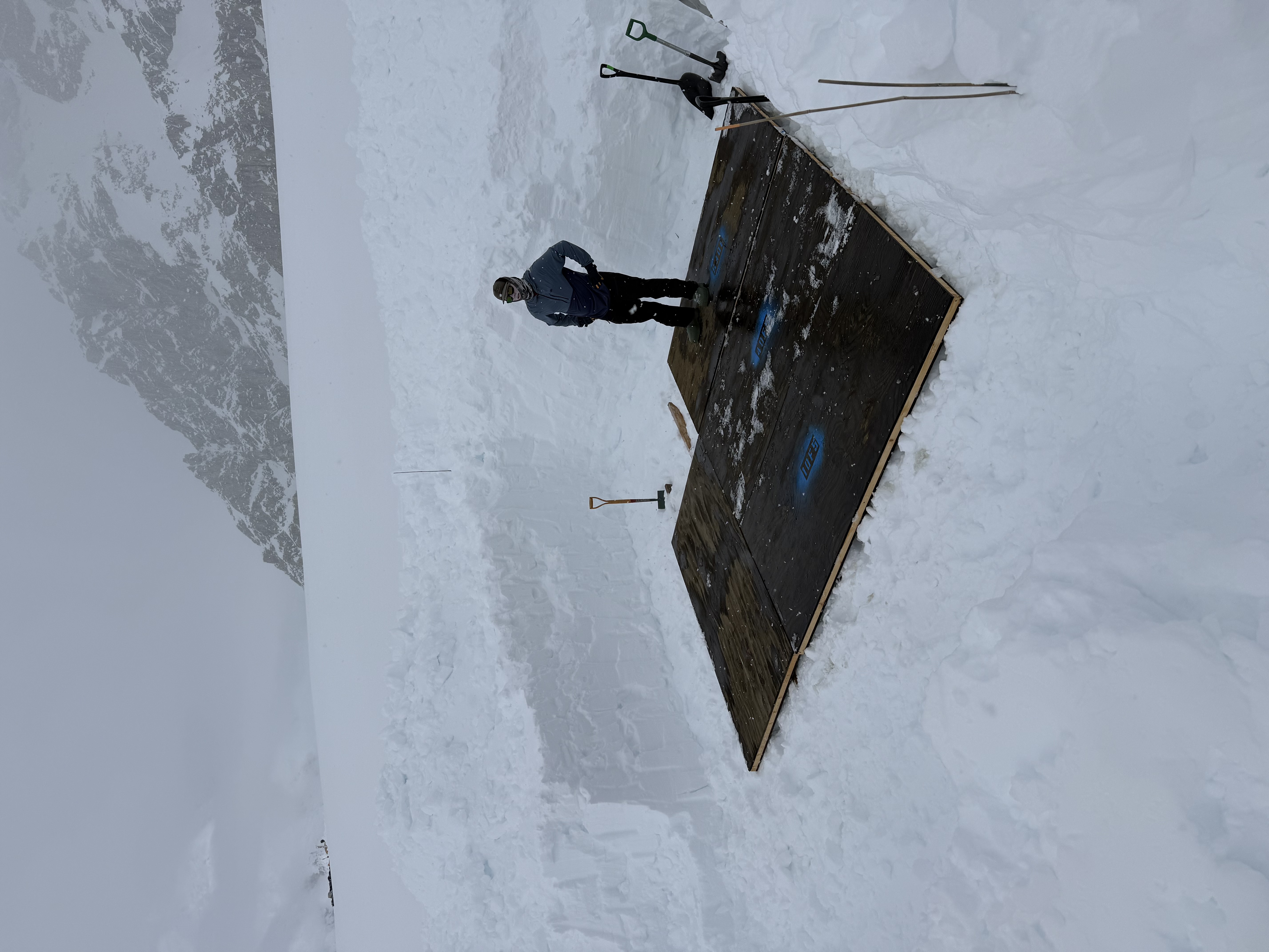 Setting up Basecamp Infrastructure A ranger stands in a large square hole dug out of the snow with black flooring covering