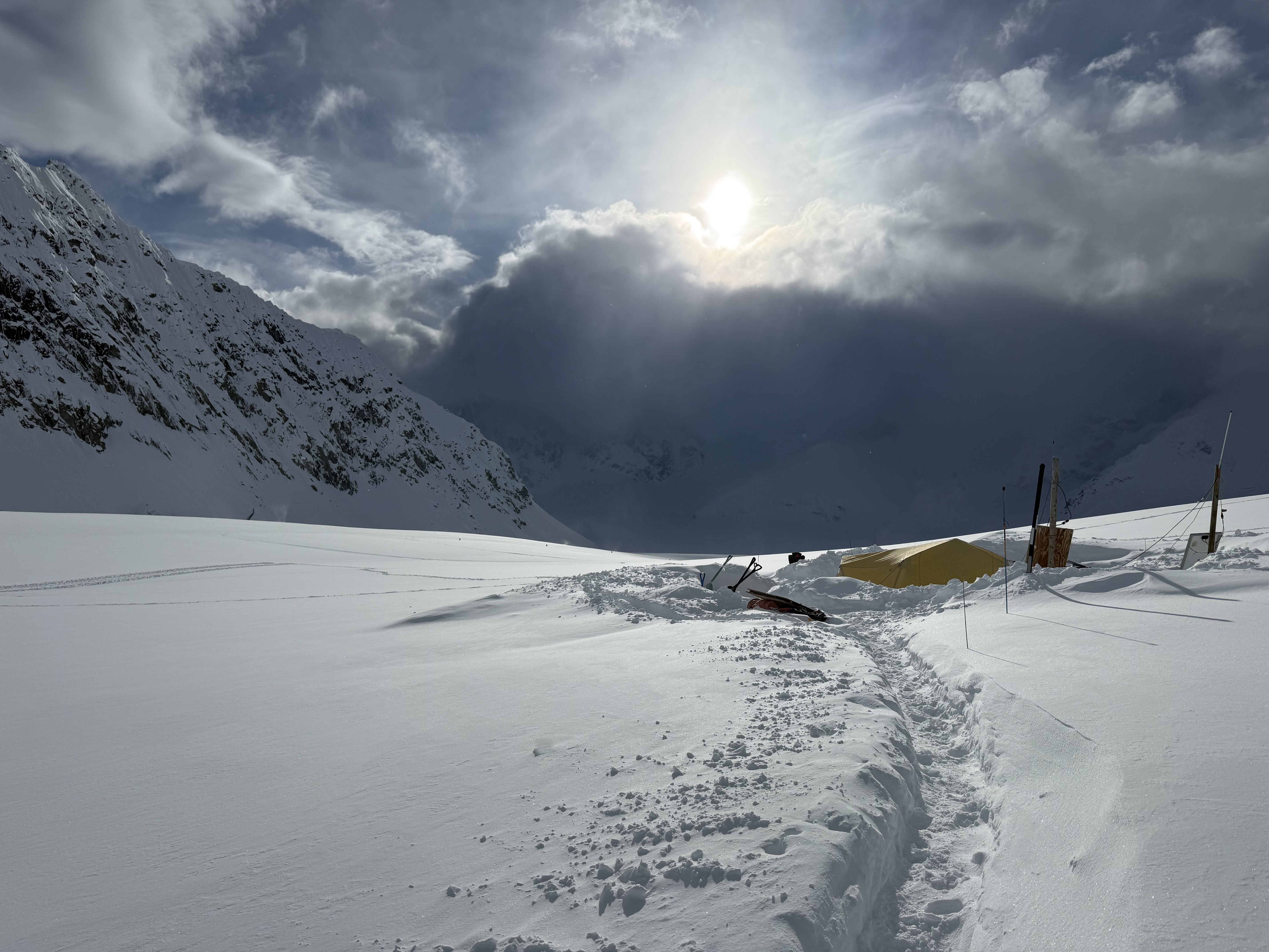 brief sun break The sun peeks above a large group of grey clouds over a snowy landscape with a trail dug