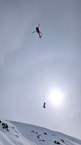 Short Haul refresher training A helicopter dangles equipment above a snowy landscape against a grey sky