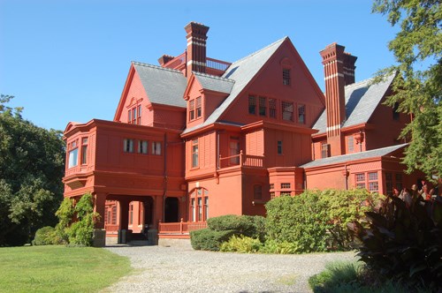 Brick red, four story mansion with multiple roofs and chimneys.