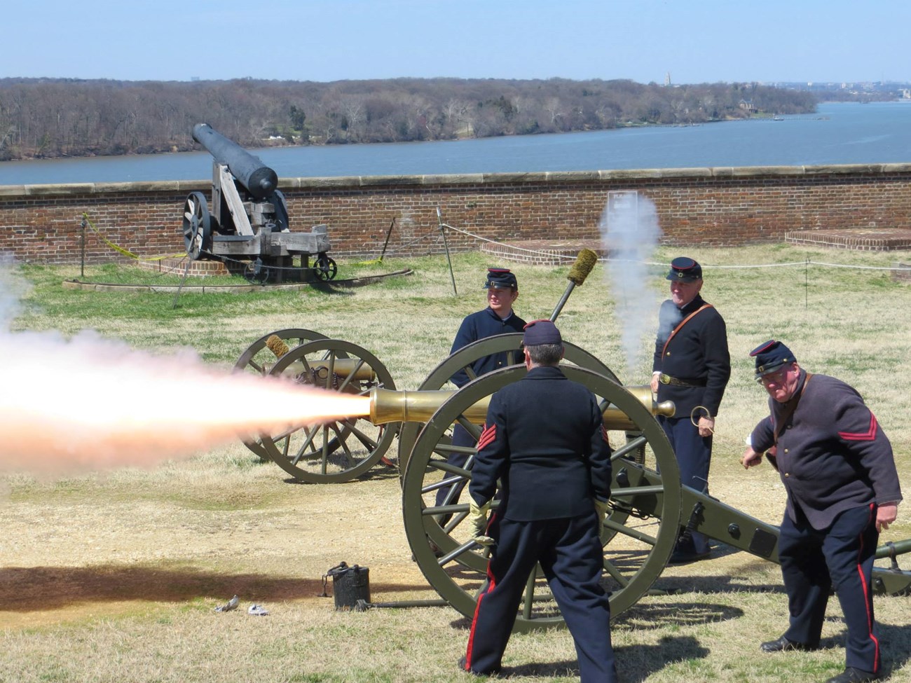 Park staff and volunteers in Civil War uniforms firing a cannon.