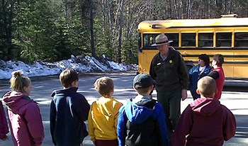 Group of students listen to ranger, with school bus parked in background