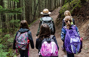 Girls with backpacks follow ranger down trail