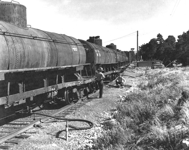 An historic black and white image of water supply train transferring water from the train to water supply tanks.