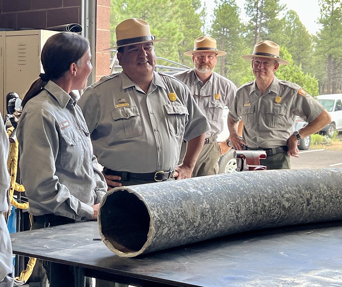 A piece of water pipe sits on a table while a uniformed park ranger shows it to the National Park Service Director.