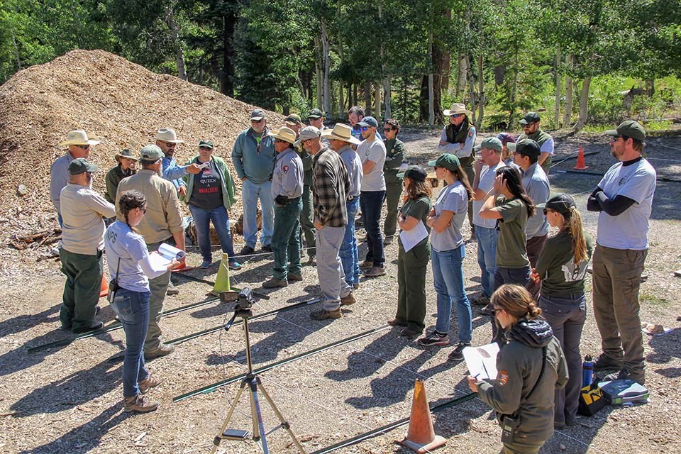 a group of around two dozen park employees gathered around in a circle and attending a morning work briefing.