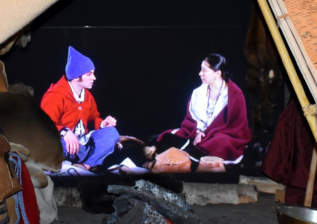 Interior of a wigwam with a monitor showing people in historic clothing.