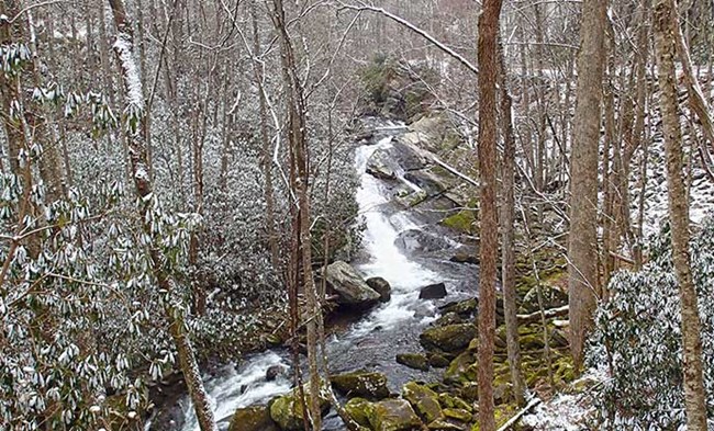 A waterfall slides over a rock outcrop in a snowy forest