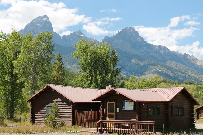 A log building with mountains towering behind.