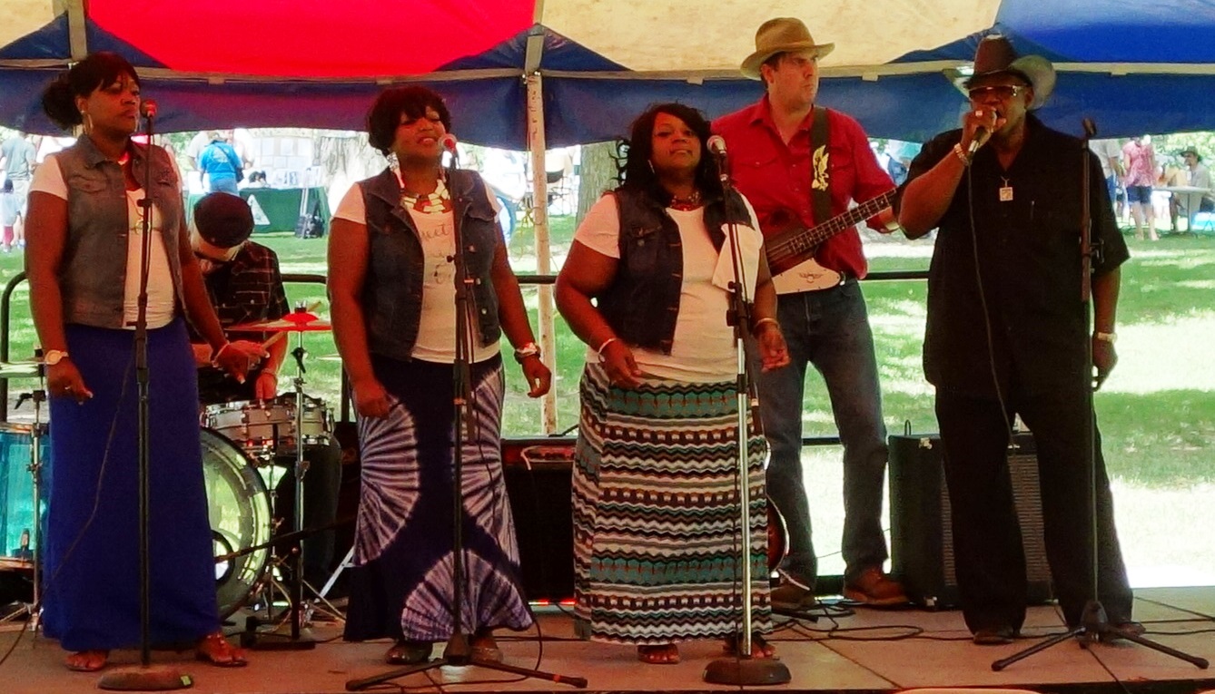 Image is a music group performing at Carver Day. The image includes 3 woman and two men singing under a tent.
