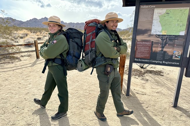 Two Rangers standing back to back  with large backpacks onand smiling