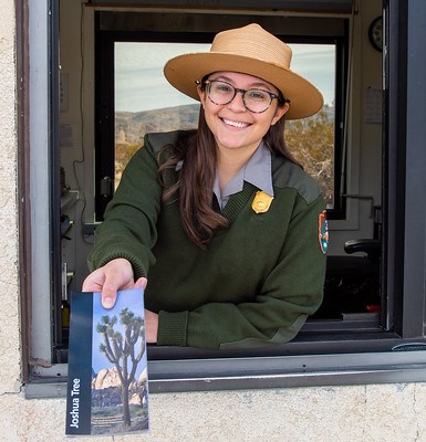 A Park Ranger smiling and holding out a map while leaning out of an entrance booth