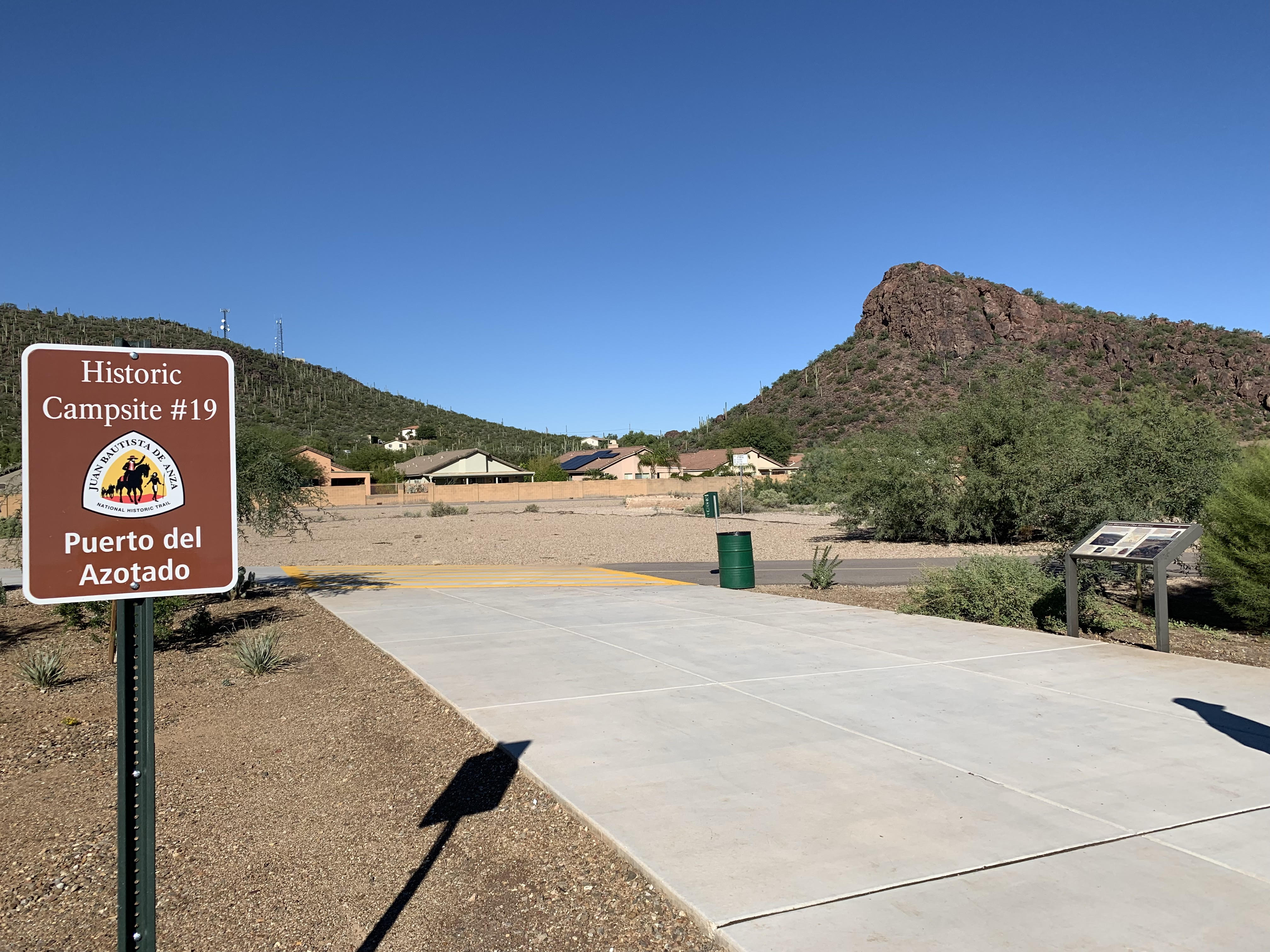 A trailhead sits at the base of the pass where the expedition travelled through. You can see the saddle of the mountains. A sign marks it as part of the Anza Trail reading A trailhead sits at the base of the pass where the expedition travelled through. You can see the saddle of the mountains. A sign marks it as part of the Anza Trail reading
