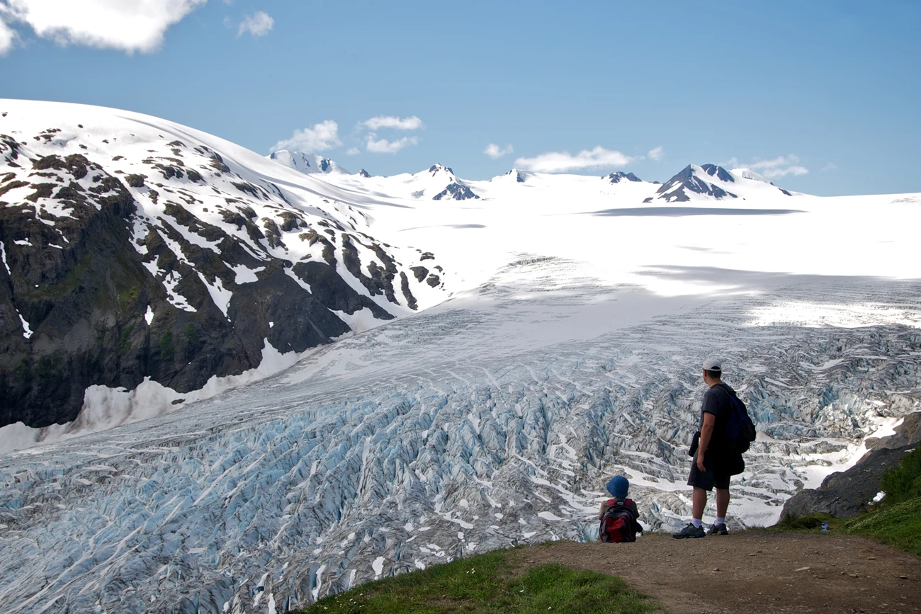 People walk down a trail with a large valley beyond