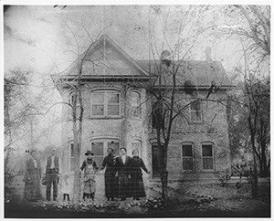 A group of settlers in front of a Victorian-style home.