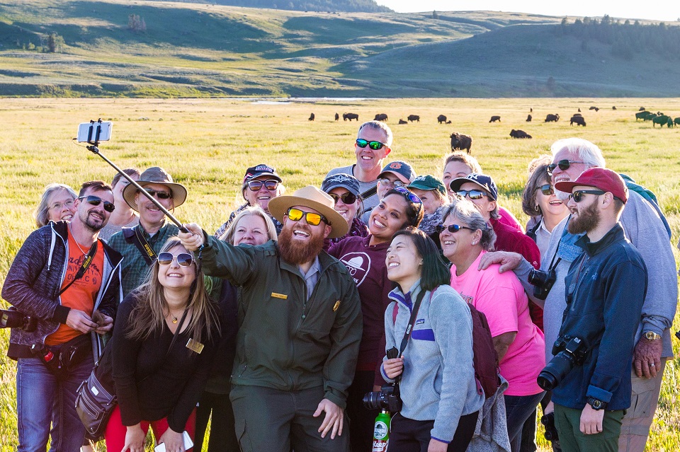 Ranger taking a selfie with a tour group with bison herd in the background