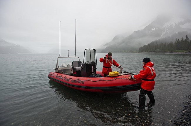 Kenai Fjords NPS researchers Nps employees dock a boat on a gravel bank.