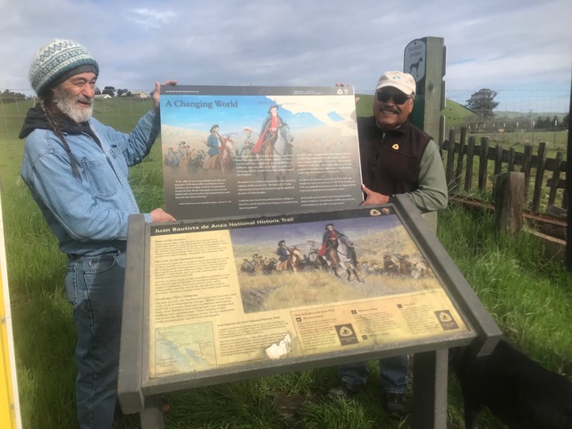 SJB Wayside replacement Two volunteers standing behind an old interpretive wayside panel and holding a new panel.