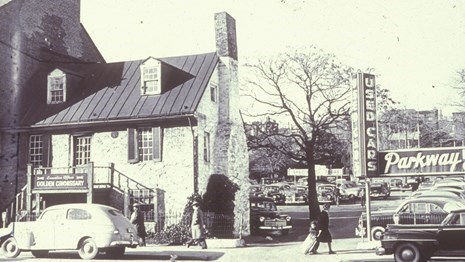 Black and white photo of old stone house with a car parked in front