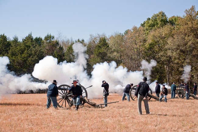 Living historians portraying Union soldiers fire a battery of cannons into an open field.