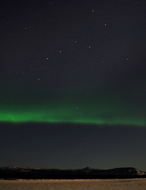 Stars of the big dipper over a green glow in the big night sky.