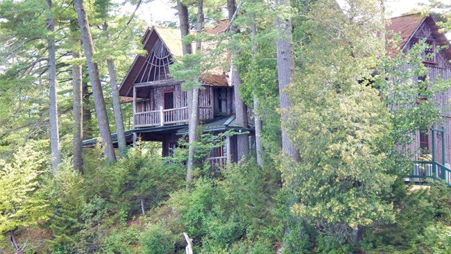 Multi-story wood cabin along the water, surrounded by forest