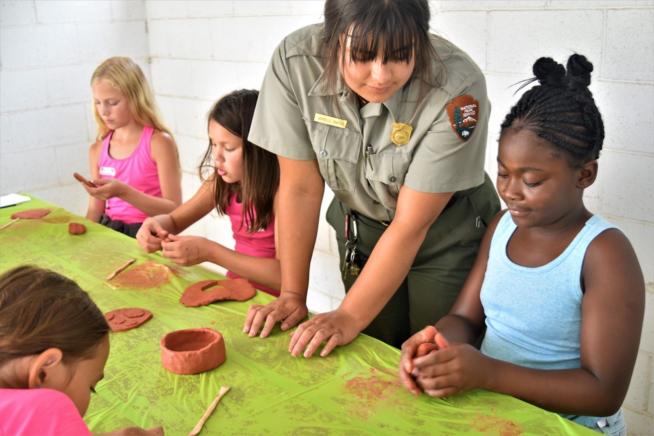 Ranger looks over pottery work of three young girls.