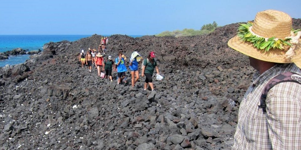 Group of people hike through lava rocks near the ocean