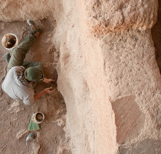 View from above of a man working on an adobe wall, with two buckets of clay nearby