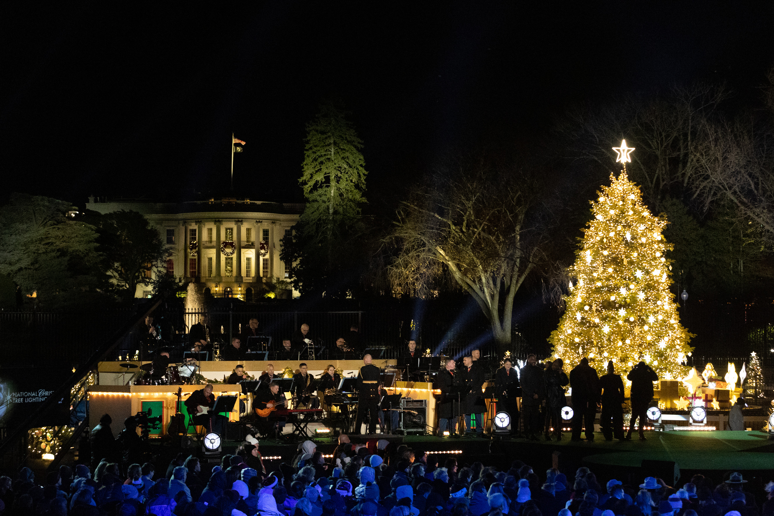 A band prepares to play in front of the White House and a large lit Christmas tree at night.