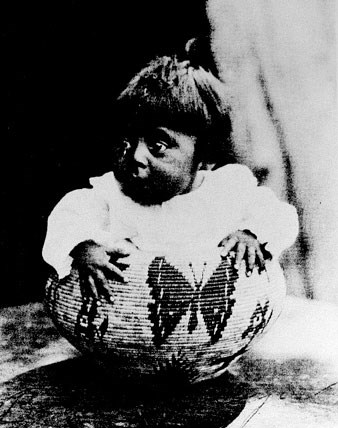 Baby sitting in a basket with a butterfly design woven onto the basket