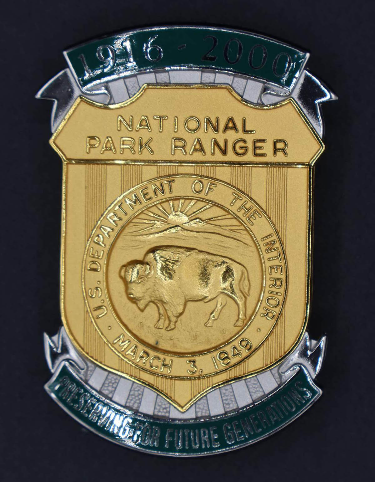 Gold shield-shaped bison badge marked National Park Ranger. Green banners at top and bottom read 1916-2000 and Preserving for Future Generations. 